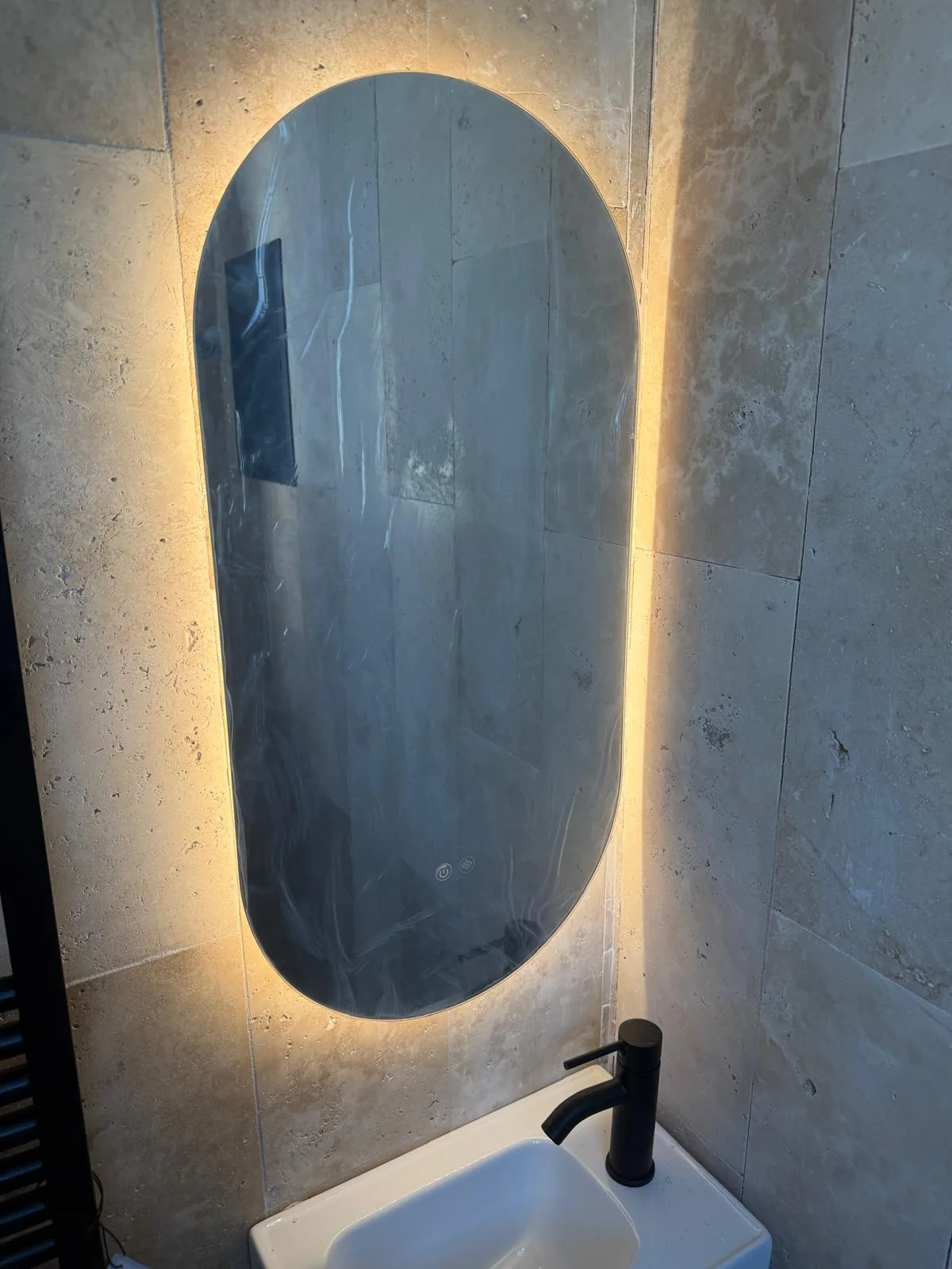 Miroir ovale rétroéclairé sur mur en travertin, robinetterie noire