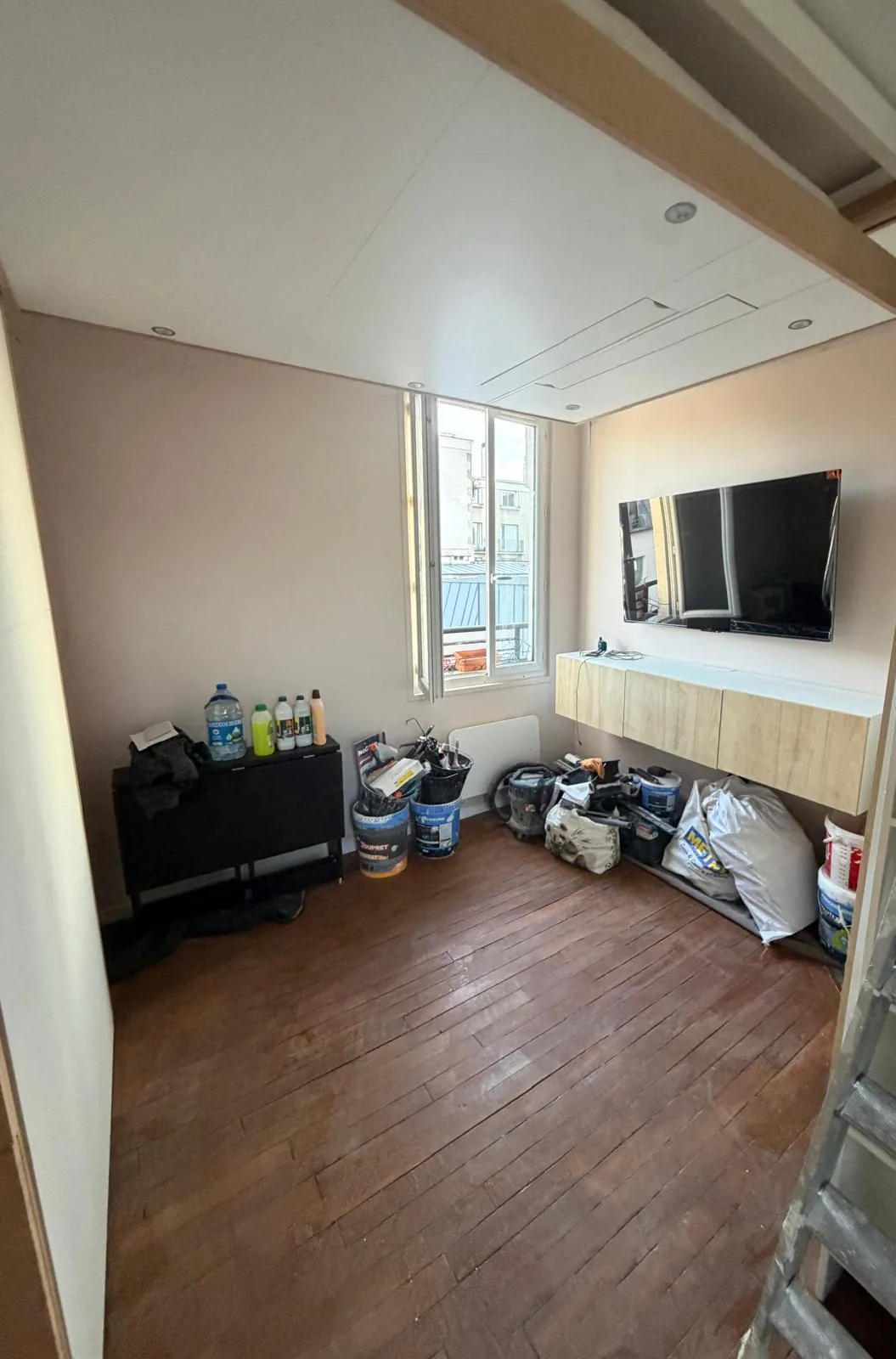 Le studio en configuration jour : meuble TV, écran mural et fenêtre sur les toits